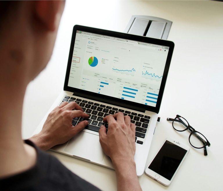 Person analysing data on a laptop, with glasses and a smartphone nearby.